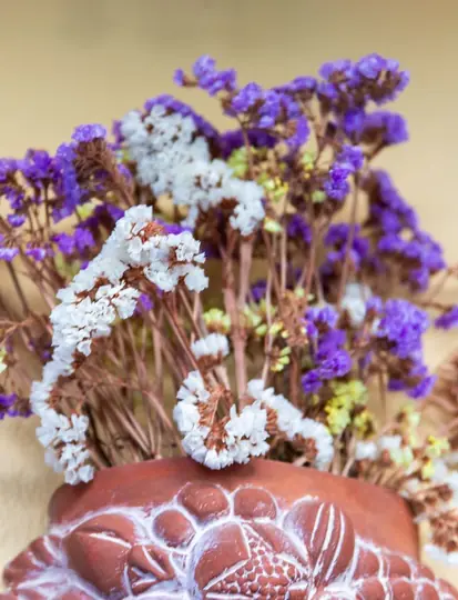 Dried purple and white flowers in a carved terracotta pot