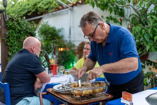 Dimitri serving a baked dish to guests at the table