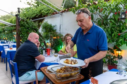 Dimitri bringing a baked dish out to guests in the garden